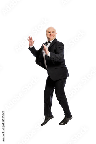 Laughing middle-aged bald man in a suit jumping. Isolated on white background, vertical.