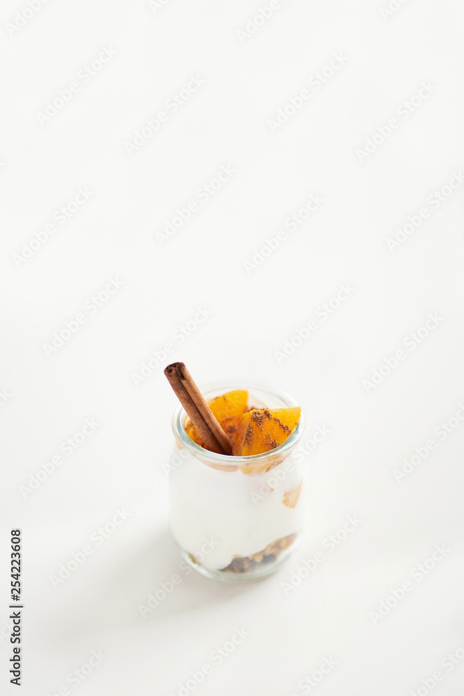 Jars of greek yogurt with granola, cinnamon and canned apricots on white background, vertical oriented Jars of greek yogurt with granola, cinnamon and canned apricots on white background, vertical oriented