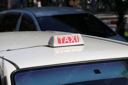 Taxi light sign or cab sign in white and red color with white text on the car roof at the street blurred background.