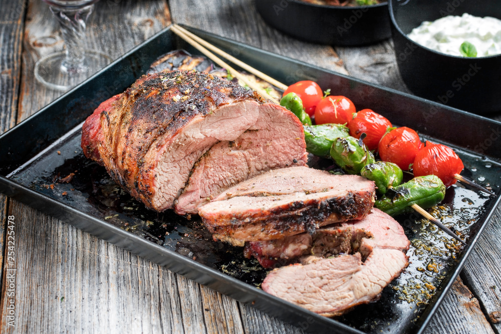 Barbecue marinated lamb roast with vegetable and tzatziki as closeup on a tray Barbecue marinated lamb roast with vegetable and tzatziki as closeup on a tray