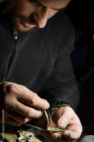 The watchmaker holds the silver case of a vintage pocket watch in his workshop
