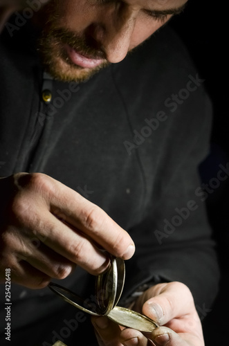 The watchmaker holds the silver case of a vintage pocket watch in his workshop