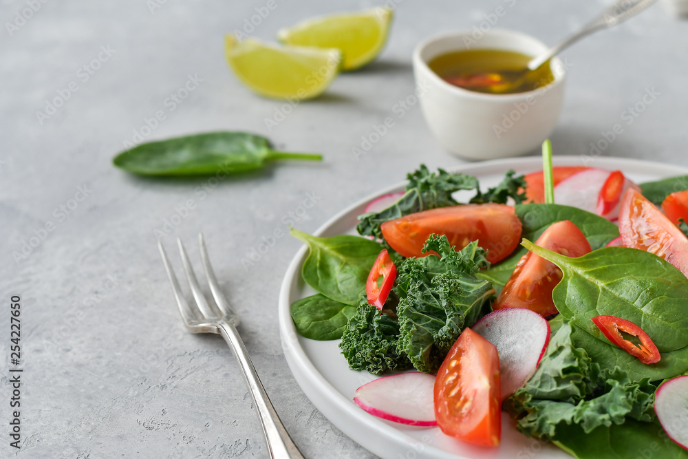 fresh salad of organic spinach, kale, red tomatoes and radish with olive oil and lime juice. healthy eating concept. diet, vegan cuisine. light background, selective focus