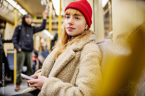 junge Frau, Mädchen, Teenager, sitzt mit ihrem Smartphone, Handy, in der U-Bahn photo