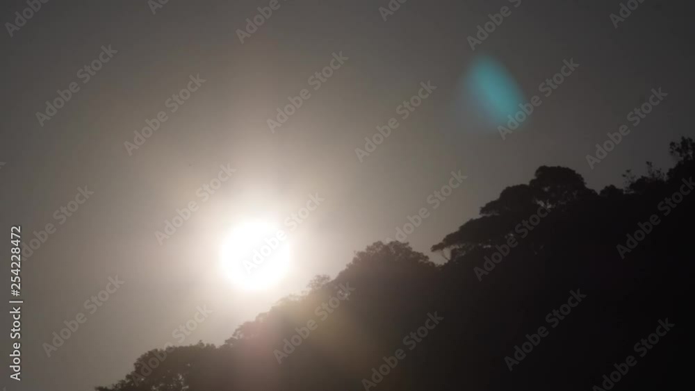 Timelapse sunset descending behind silhouette of lush foliage on hillside skyline as clouds pass behind. Timelapse sunset descending behind silhouette of lush foliage on hillside skyline as clouds pass behind.