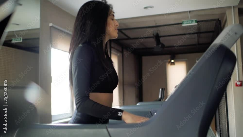 attractive girl of Caucasian appearance runs on a treadmill. active brunette girl in the gym switches the speed on the treadmill. athlete cardio activity on a treadmill attractive girl of Caucasian appearance runs on a treadmill. active brunette girl in the gym switches the speed on the treadmill. athlete cardio activity on a treadmill