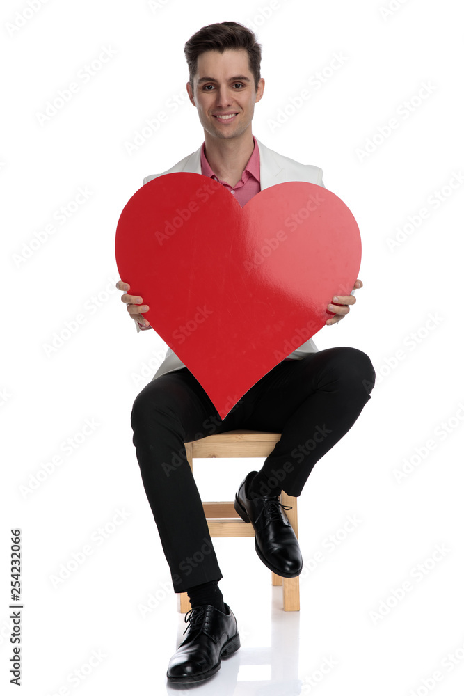 smiling young smart casual man sitting and holding a heart smiling young smart casual man sitting and holding a heart