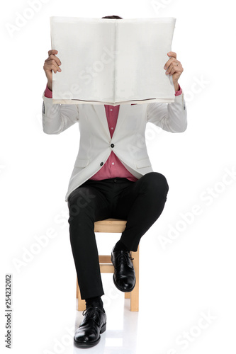 seated elegant man holding paper over his face