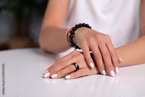 Closeup model hands with manicure, white nails, black ring with stone, bracelet made of shiny black beads, red, beige braided thread on the wrist. Concept fashion shot in studio jewelry store