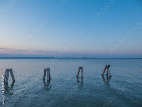 Soft colors of a sunset on the lake. pillars coming out of the calm water. Pillars in groups of three, form shapes of  pyramids. Calm surface of the lake. Mountains in the back. Pinky sky. photo