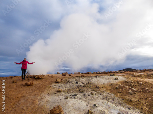 Girl wearing pink jacket stands in front of a smoking pool, filled with sulfur. She spreads her arms, in a gesture of being unable to get over bad smell, she cannot do anything. Thick and dense smoke