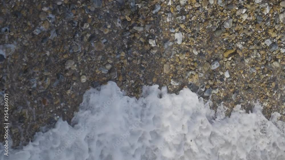 Waves coming in and out on stony beach, birds eye view in slow motion Waves coming in and out on stony beach, birds eye view in slow motion