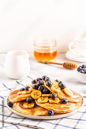 Pancakes with banana, blueberries on white plate.
