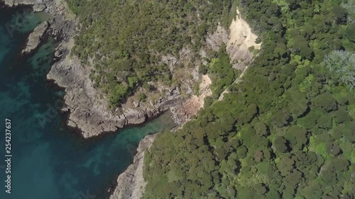 A slow moving aerial drone shot that pivots around a carved out rock face in a tropical paradise with crystal clear ocean waters below. photo