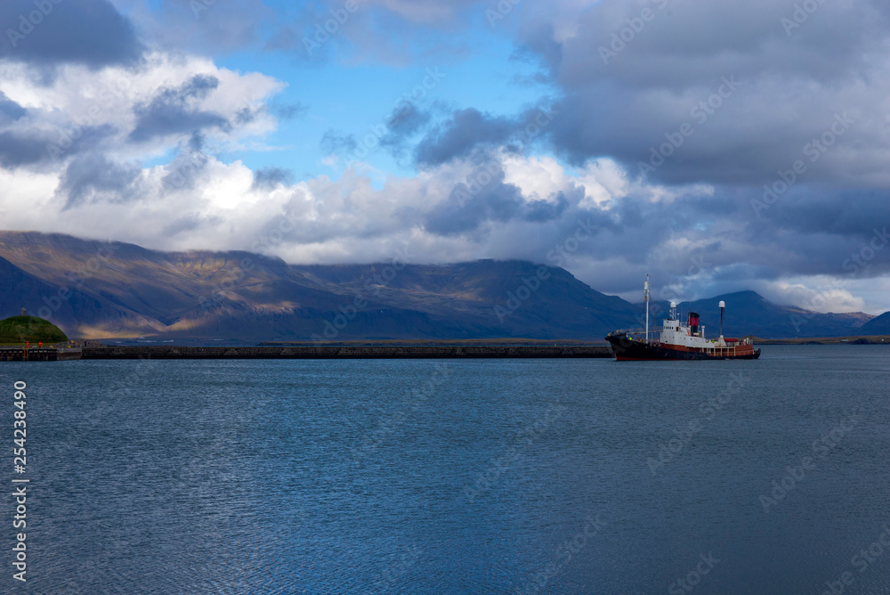 Ship against the backdrop of picturesque mountains and rain clouds entering the bay of the port of Reykjavik, Iceland