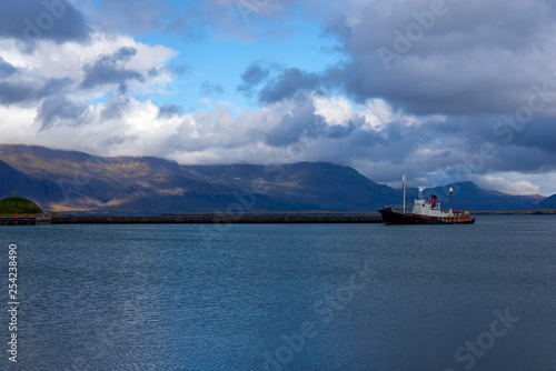 Ship against the backdrop of picturesque mountains and rain clouds entering the bay of the port of Reykjavik, Iceland