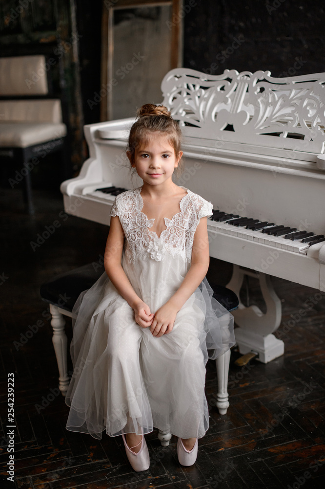 Portrait of a beautiful girl in a white dress near the piano
