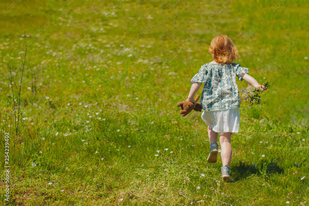 Cute cheerful redhead girl playing on the meadow, field. Beautiful little girl in the meadow near sunflowers and smiling. Soft sunlight. Cute cheerful redhead girl playing on the meadow, field. Beautiful little girl in the meadow near sunflowers and smiling. Soft sunlight.
