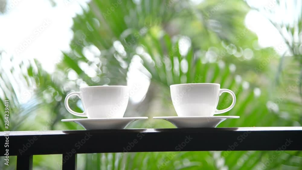 A static shot of two white cups of coffee, outside with smooth green bokeh in the background. A static shot of two white cups of coffee, outside with smooth green bokeh in the background.