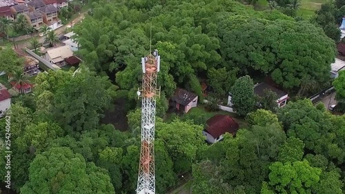 Aerial shot of a cellphone tower in a small city of a rural area with some green environment with a lot of nature and small houses photo