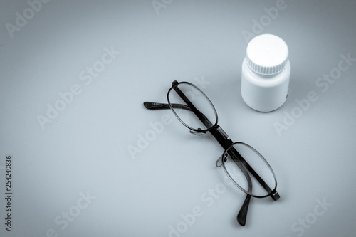 Black and white photo of glasses lying near white pills bottle with vignette effect. Concept of eyesight