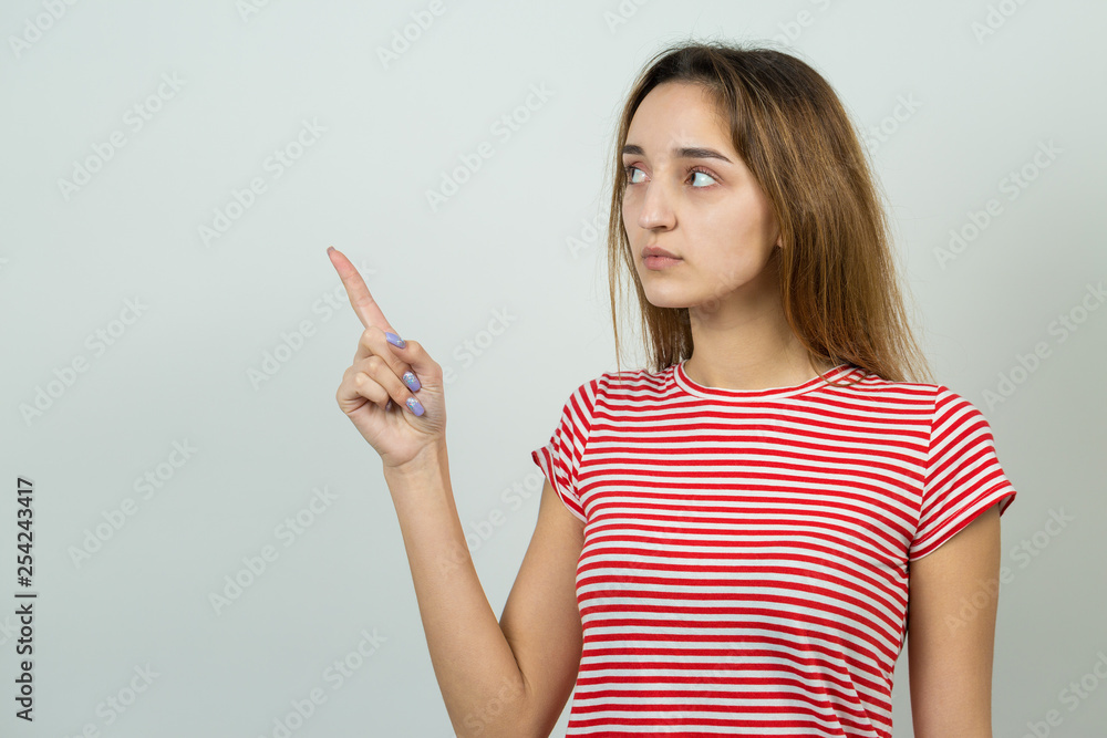 Happy young caucasian female in a striped red T-shirt pointing fingers away, showing copy space for your text. Happy young caucasian female in a striped red T-shirt pointing fingers away, showing copy space for your text.