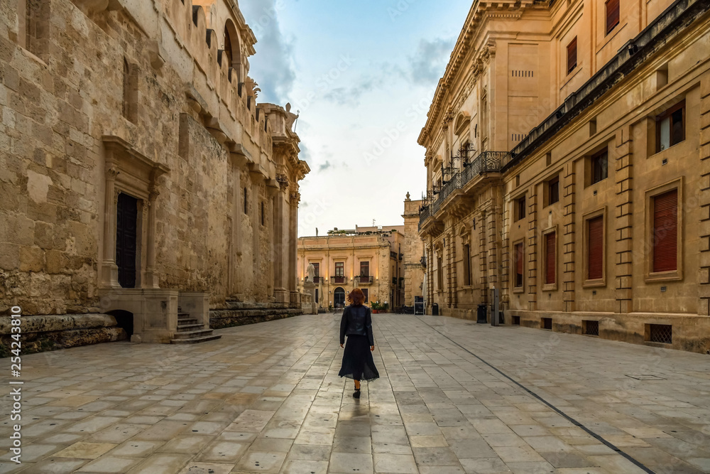 Young woman walking across the main street of the island Ortigia in the early morning, Syracuse in Sicily, Italy