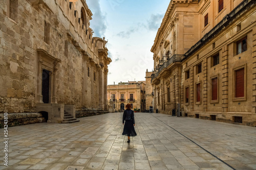 Young woman walking across the main street of the island Ortigia in the early morning, Syracuse in Sicily, Italy © Andrii Shnaider