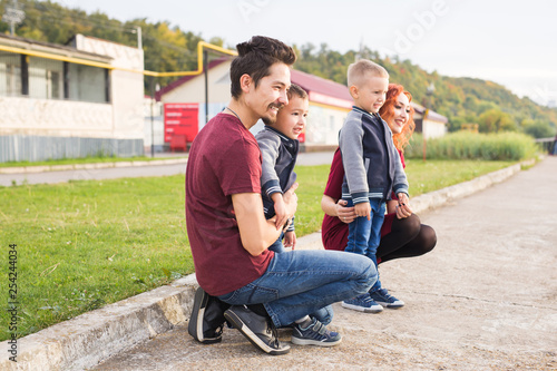 Parenthood, childhood and family concept - Parents and two male children walking at the park and looking on something