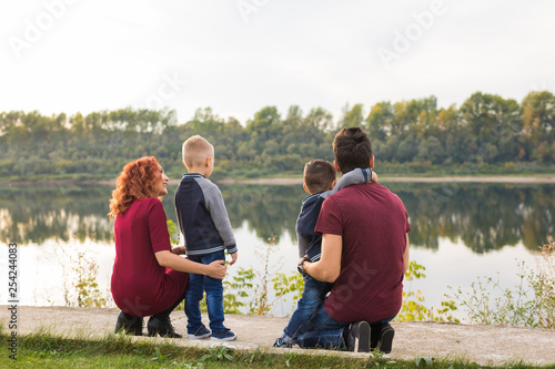 Parenthood, childhood and family concept - Parents and two male children walking at the park and looking on something, back view