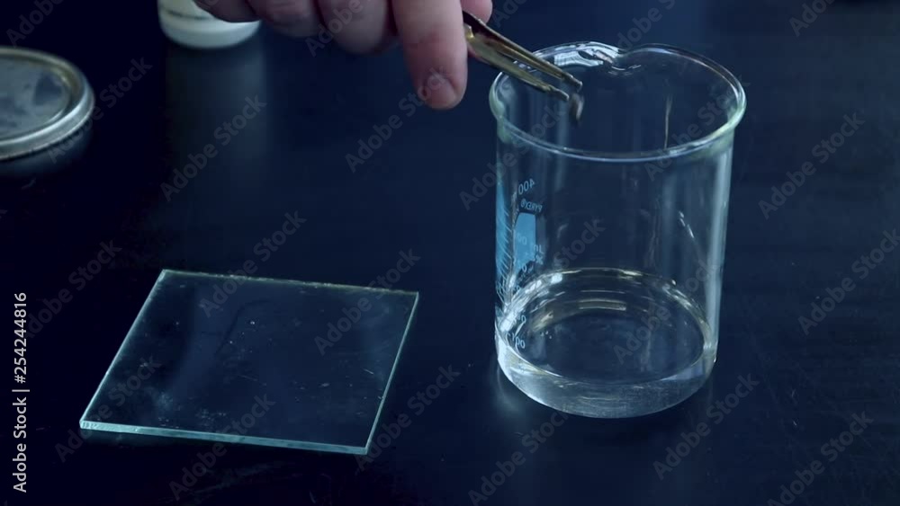 A small piece of sodium metal being added to a glass beaker with water and reacts vigorously to produce flamable hydrogen gas that is lit by a burning splint