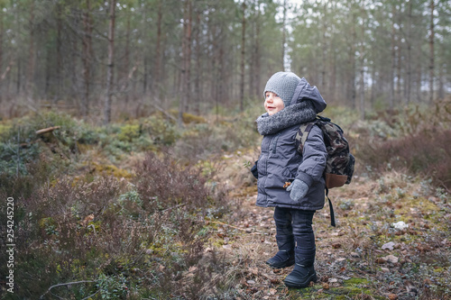 Little boy go hiking with backpack on the forest on a cold day