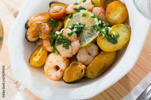 Tasty warm salad with fried potatoes, shrimp and mussels, served at plate