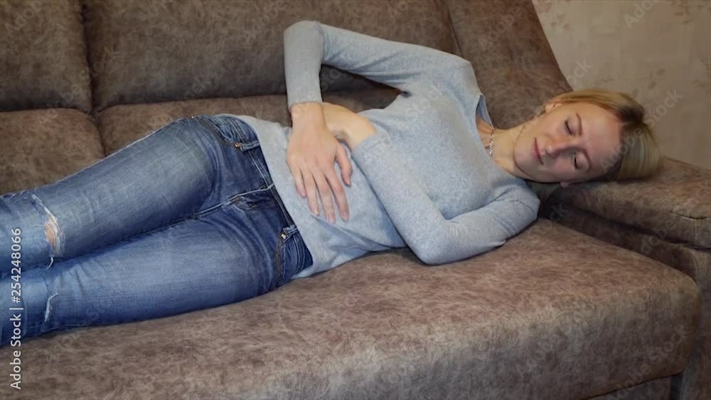 Slow movement sick woman having a stomach ache hands touching belly release painful lying on couch resting at home. young girl wake up while taking nap because abdomen pain. lady feel uncomfortable Slow movement sick woman having a stomach ache hands touching belly release painful lying on couch resting at home. young girl wake up while taking nap because abdomen pain. lady feel uncomfortable