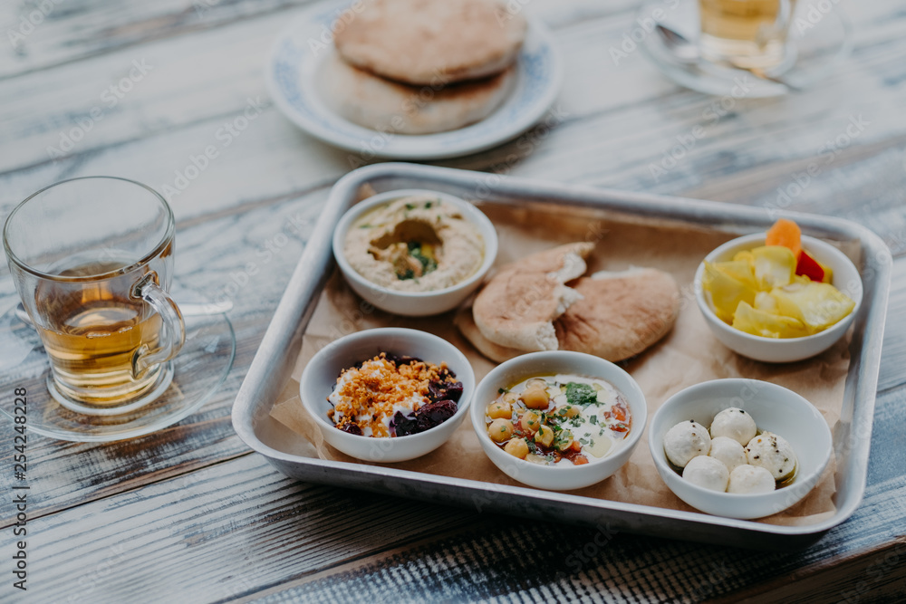Overhead image of traditional Israel food on tray. Hummus, domestic goat cheese, tomatoe core, beetroot with spices, pita bread, beverage in glass Overhead image of traditional Israel food on tray. Hummus, domestic goat cheese, tomatoe core, beetroot with spices, pita bread, beverage in glass