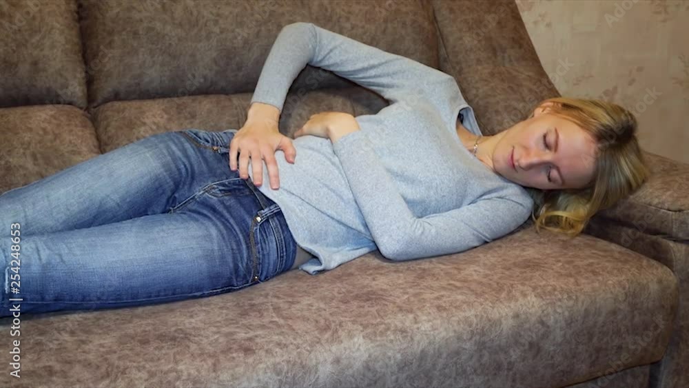 Slow movement sick woman having a stomach ache hands touching belly release painful lying on couch resting at home. young girl wake up while taking nap because abdomen pain. lady feel uncomfortable Slow movement sick woman having a stomach ache hands touching belly release painful lying on couch resting at home. young girl wake up while taking nap because abdomen pain. lady feel uncomfortable