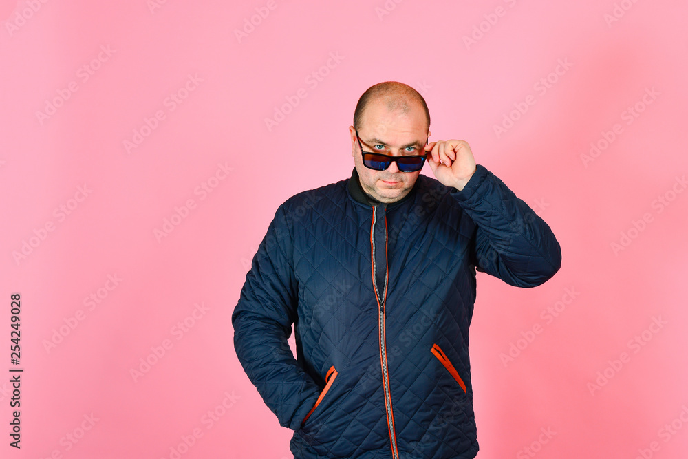 A man in a blue jacket and sunglasses on a pink background in the studio A man in a blue jacket and sunglasses on a pink background in the studio