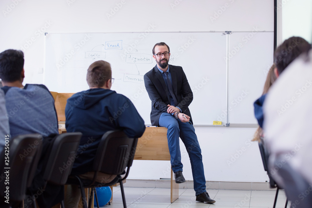 Group of students study with professor in modern school classroom. Male professor explain to students and interact with them, helping a students during class. Group of students study with professor in modern school classroom. Male professor explain to students and interact with them, helping a students during class.