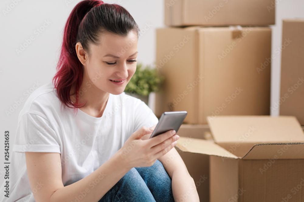 Young beautiful girl with colored hair in a white T-shirt and jeans, talking on the phone and writes messages against the background of cardboard boxes and things. Young beautiful girl with colored hair in a white T-shirt and jeans, talking on the phone and writes messages against the background of cardboard boxes and things.