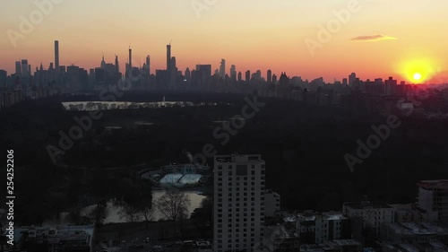 Epic drone flight into New York City's Central Park from the Harlem neighborhood at gorgeous sunset golden hour.  Ice skaters and ball fields come into view.  in 4K.