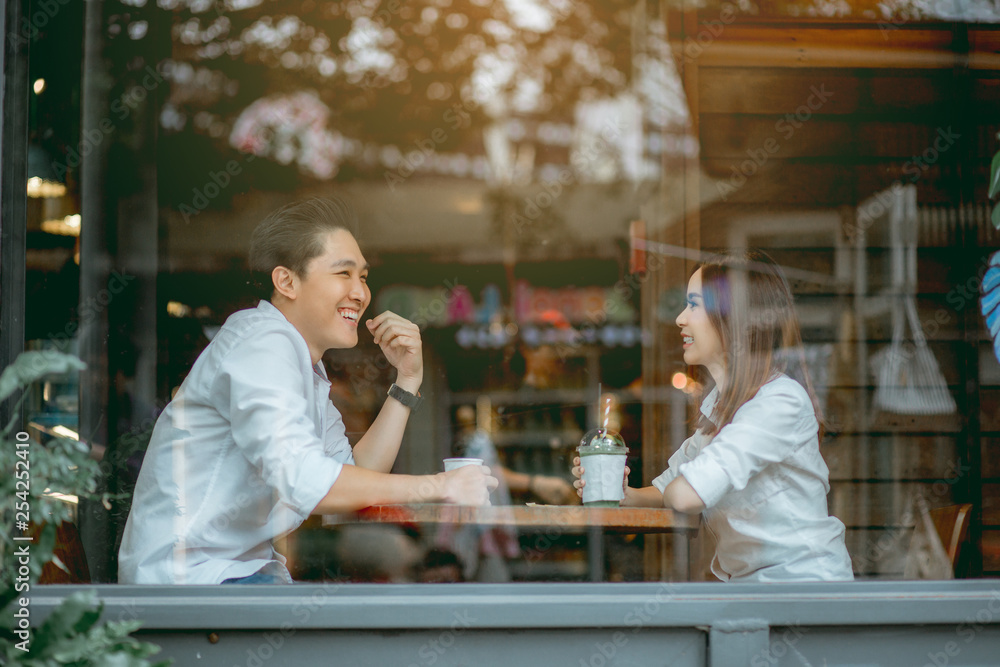 Asian couple talking happily in the cafe during the daytime. - obrazy, fototapety, plakaty 