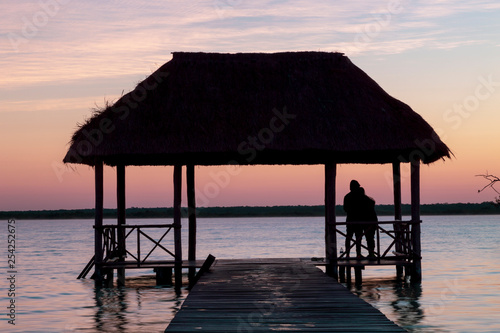 Fototapeta Naklejka Na Ścianę i Meble -  Bacalar, Mexico -January 20,2019; Friends watching the sunset at the pier of the Bacalar Lagoon(lagoon of the seven colors) Quintana Roo Mexico