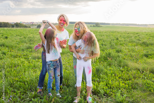 Friendship, Indian holidays and people concept - young women and children having fun on the summer field on festival of holi