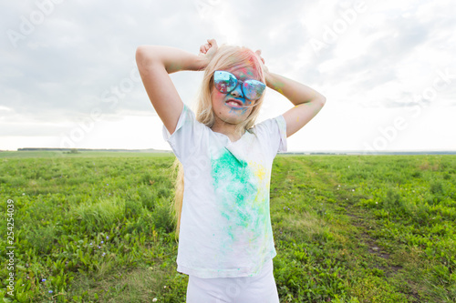 Children, festival of holi and holidays concept - happy little girl wearing sunglasses covered with color powder smiling over nature background photo