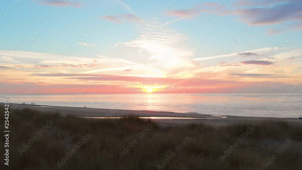 A calm low tide at the beach near the Stormsurge barrier in the south west of the Netherlands, during sunset. Smooth dynamic aerial shots. Forward revealing shot behind the dunes to the sea. A calm low tide at the beach near the Stormsurge barrier in the south west of the Netherlands, during sunset. Smooth dynamic aerial shots. Forward revealing shot behind the dunes to the sea.