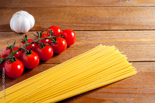 Spaghetti, cherry tomatoes and garlic on a brown wooden table. Tomatoes and garlic to the left of spaghetti.