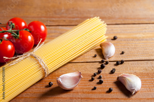 Bunch of raw spaghetti tied with rope, tomatoes cherry, slices of garlic and pepper on brown wooden background.