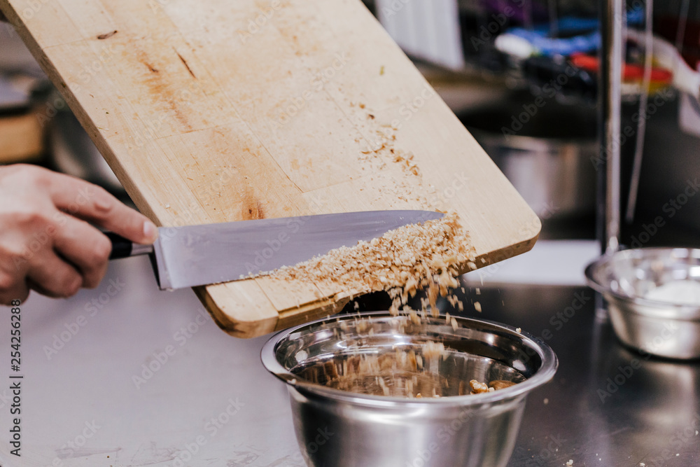 close up view of woman hand cutting nuts with knife and adding them into a bowl for a recipe. bakery concept close up view of woman hand cutting nuts with knife and adding them into a bowl for a recipe. bakery concept
