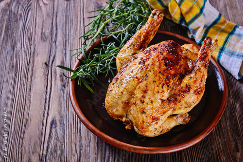 Delicious, freshly baked, crispy, baked chicken is appetizing served on a ceramic dish next to a sprig of fragrant rosemary