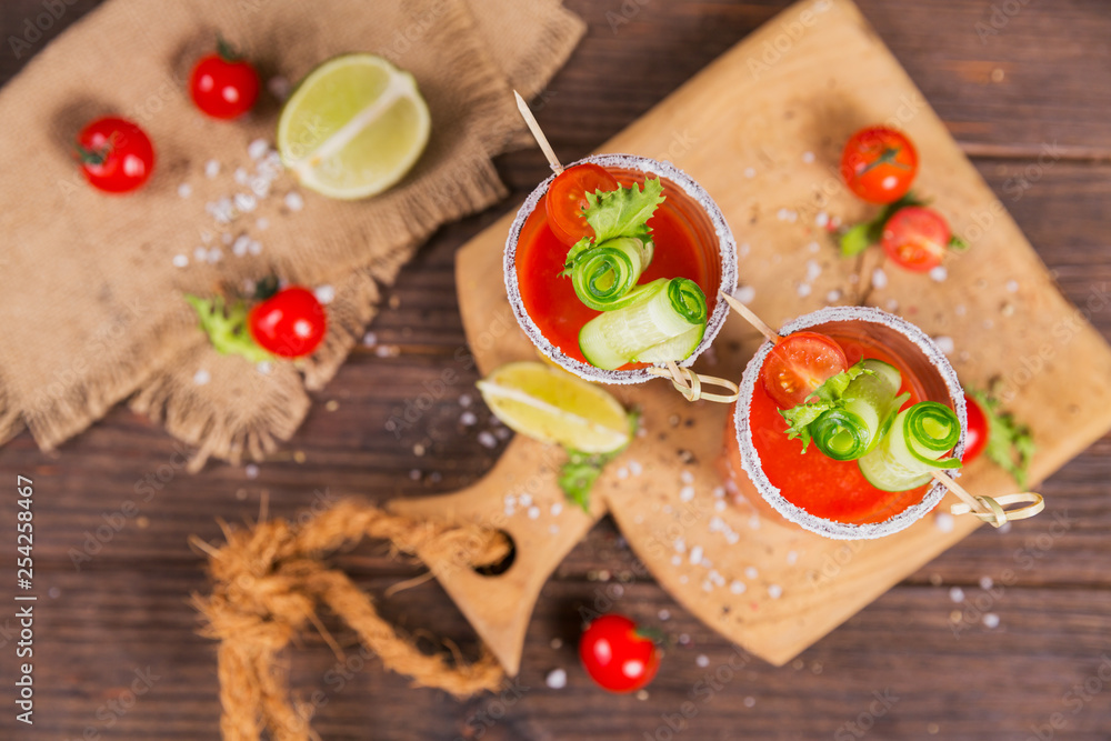 Two glasses of tomato juice decorated with fresh tomatoes, cucumber and leaves on a wooden background Two glasses of tomato juice decorated with fresh tomatoes, cucumber and leaves on a wooden background